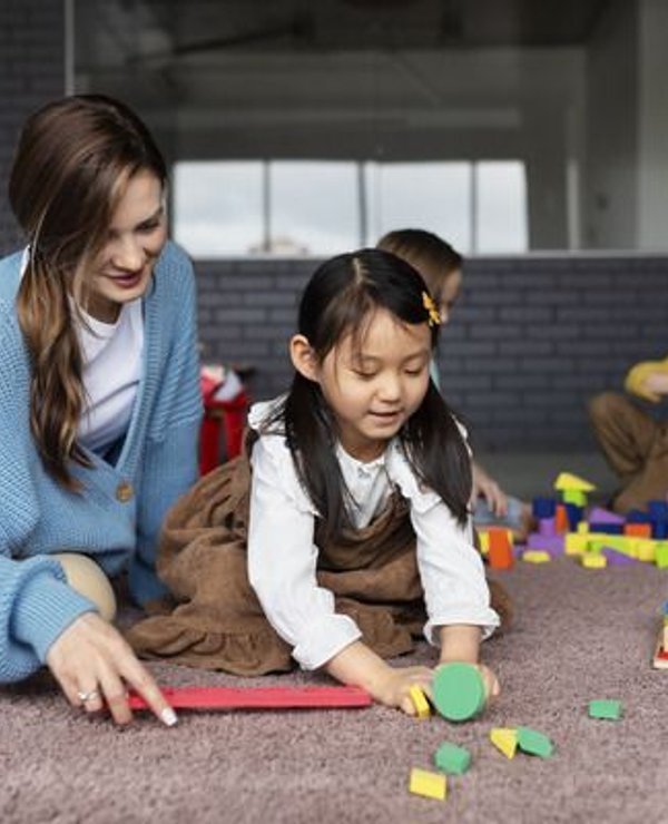 Teacher kneeling on the floor playing alongside a young girl