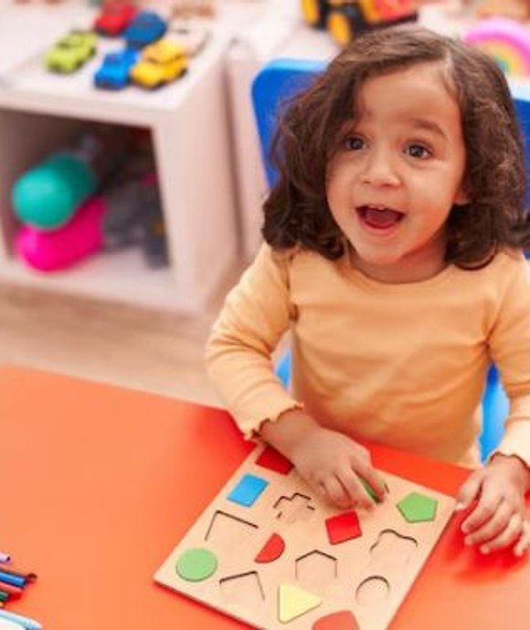 Smiling toddler fitting shapes into a wooden puzzle