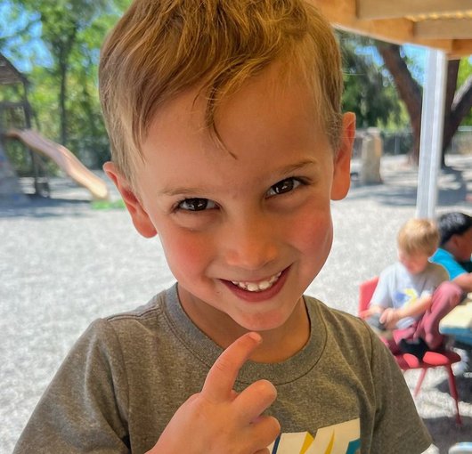 Smiling preschooler pointing at the camera in the backyard