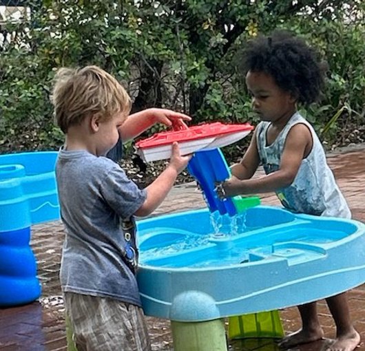 Two children playing at the water table outside