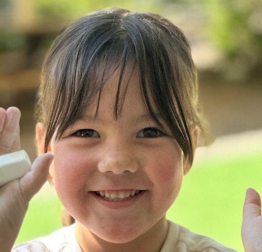 Preschooler smiling as she holds up her finished art project