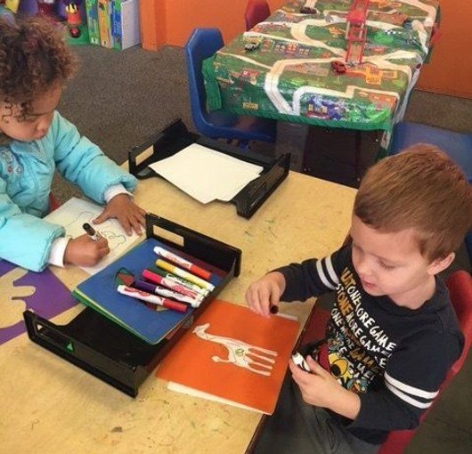 Preschoolers practising writing with markers at a desk