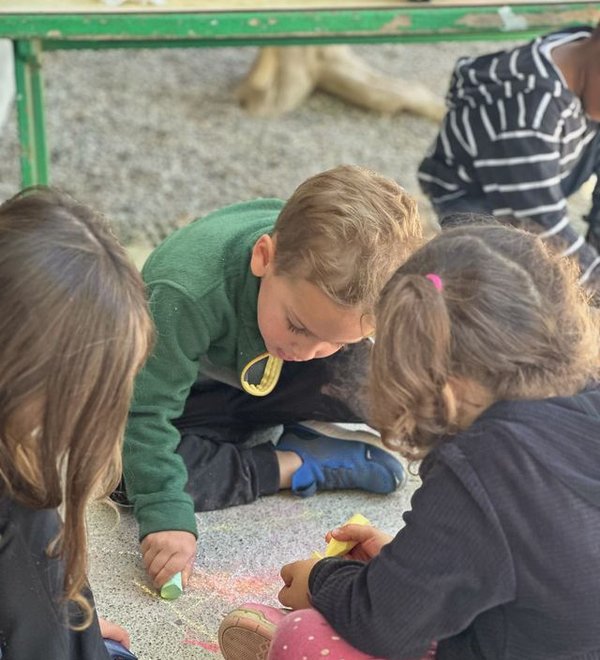 Preschoolers kneeling on the floor drawing together with colored chalk