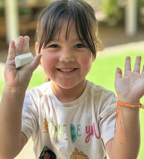 Smiling preschooler holding up a piece of chalk in the play yard