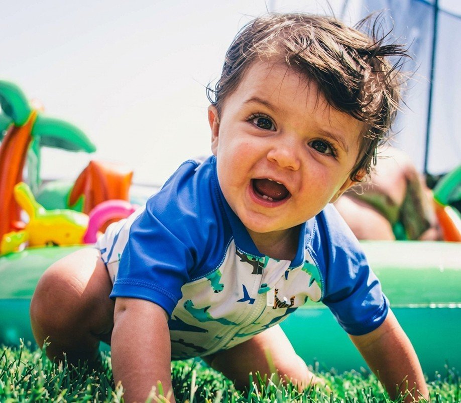 Smiling toddler crawling across the grass at Super Kidz Club