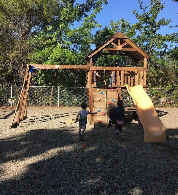 Wooden play structure with a slide in the fenced yard at Super Kidz Club