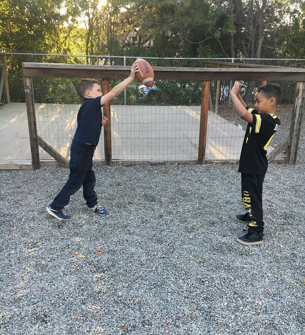 Two school-age boys tossing a football in the fenced play yard at Super Kidz Club