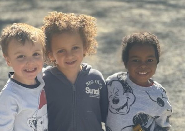 Three smiling friends standing arm in arm outdoors in the sunshine