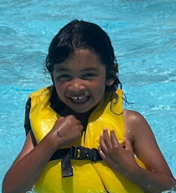 Smiling girl in a yellow life vest splashing in a swimming pool