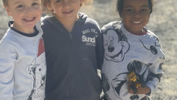 Three young friends smiling together outdoors at Super Kidz Club