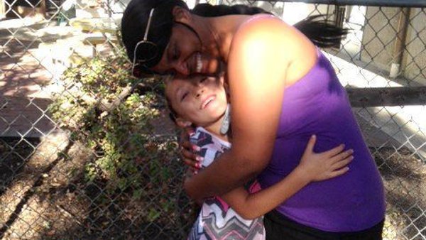 Caregiver hugging a preschooler in the yard at Super Kidz Club