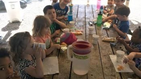 Children of mixed ages gathered around an outdoor table at Super Kidz Club