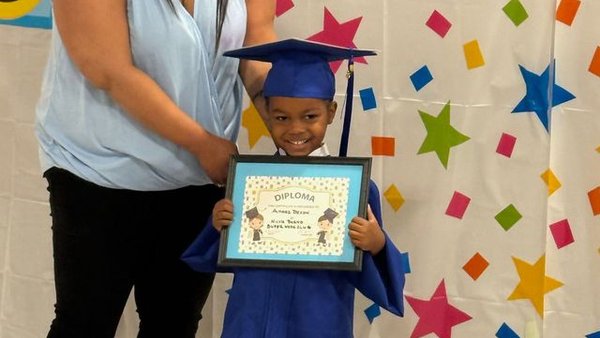 Preschool graduate in cap and gown holding a certificate with a teacher